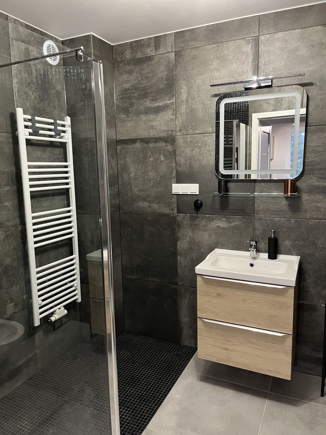 Badezimmer mit Dusche, Handtuchheizkörper und Waschtisch mit Unterschrank